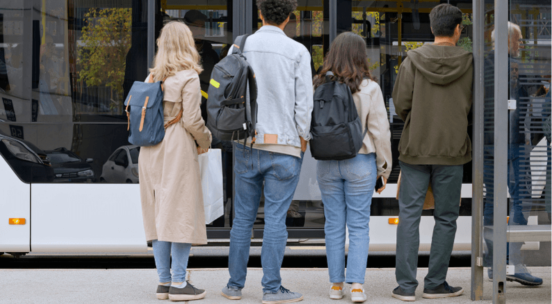 Group of people waiting at a bus stop, facing the bus parked in front of them