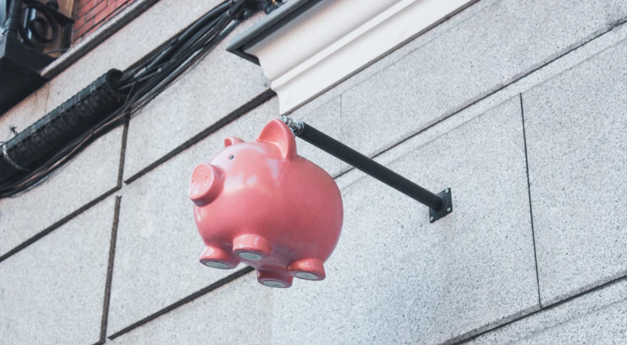 Stone brick wall with a piggy bank suspended on a metal rod protruding from the wall