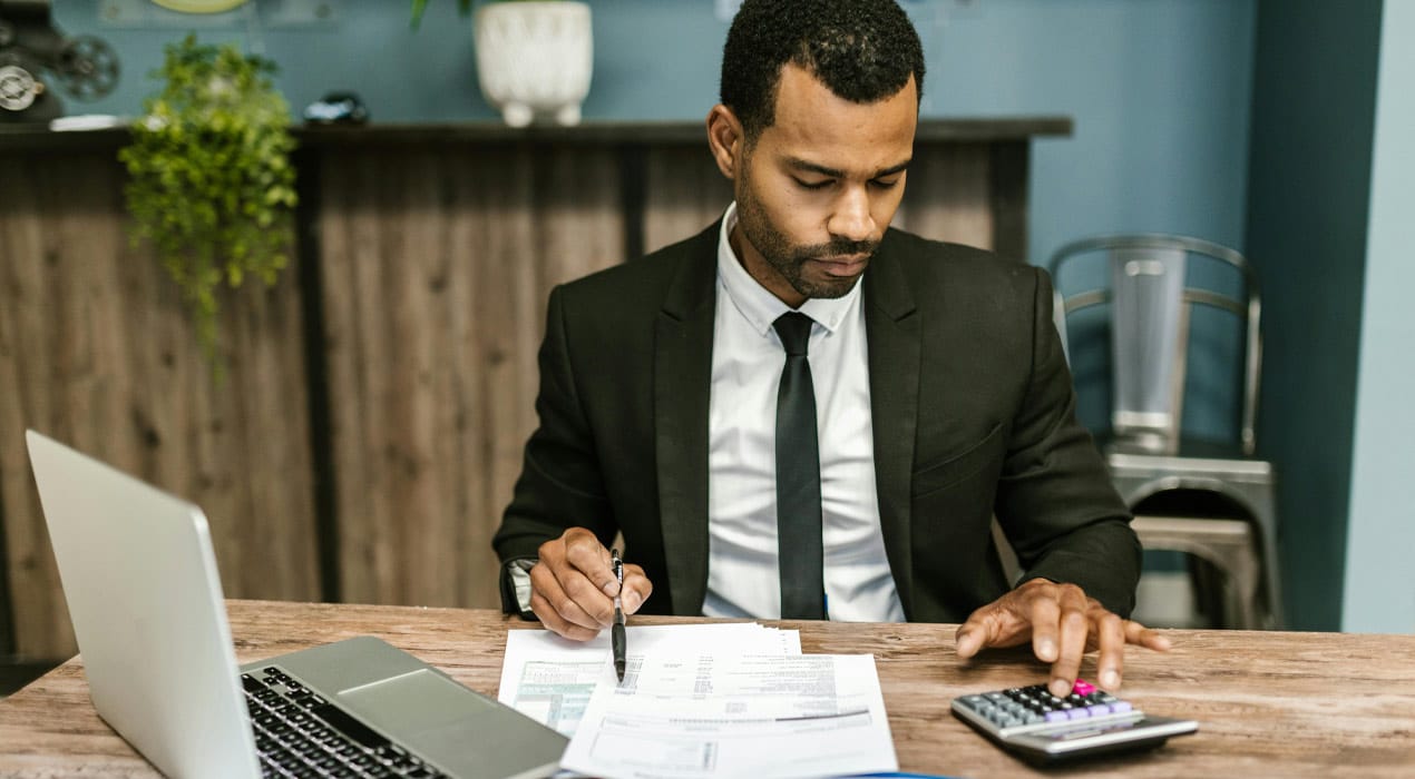 Man sitting at a desk with a laptop and papers doing calculations