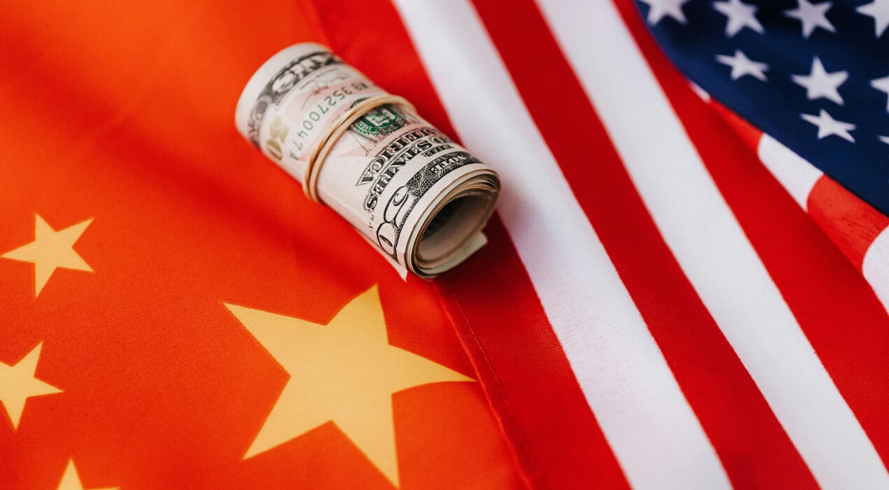Roll of US bank notes resting on the US and Chinese flags, laying side by side.