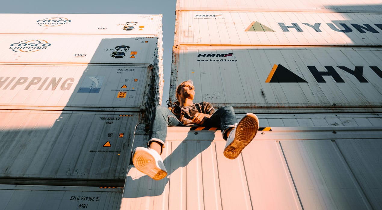 Man sitting on top of a shipping container, with others stacked behind him