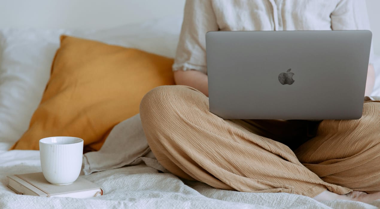 Person sitting on couch with laptop in their lap and a hot drink sitting next to them