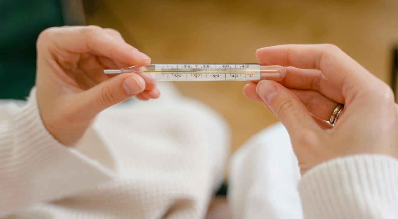 Person holding a thermometer showing a perfect 37C reading