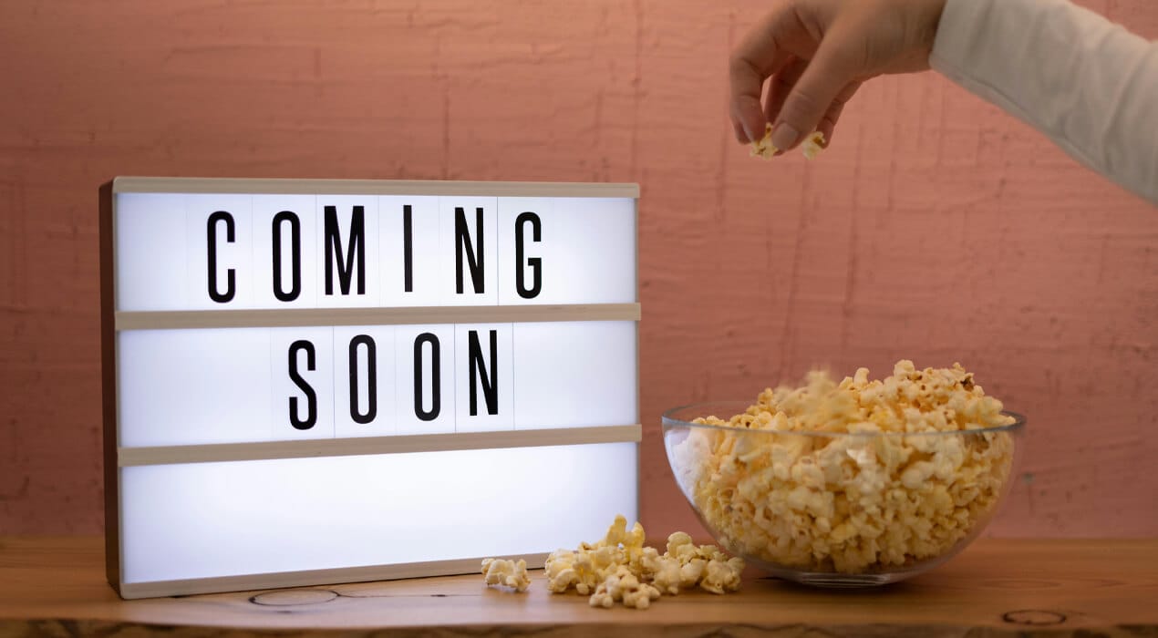 Coming Soon sign with person reaching into bowl of popcorn
