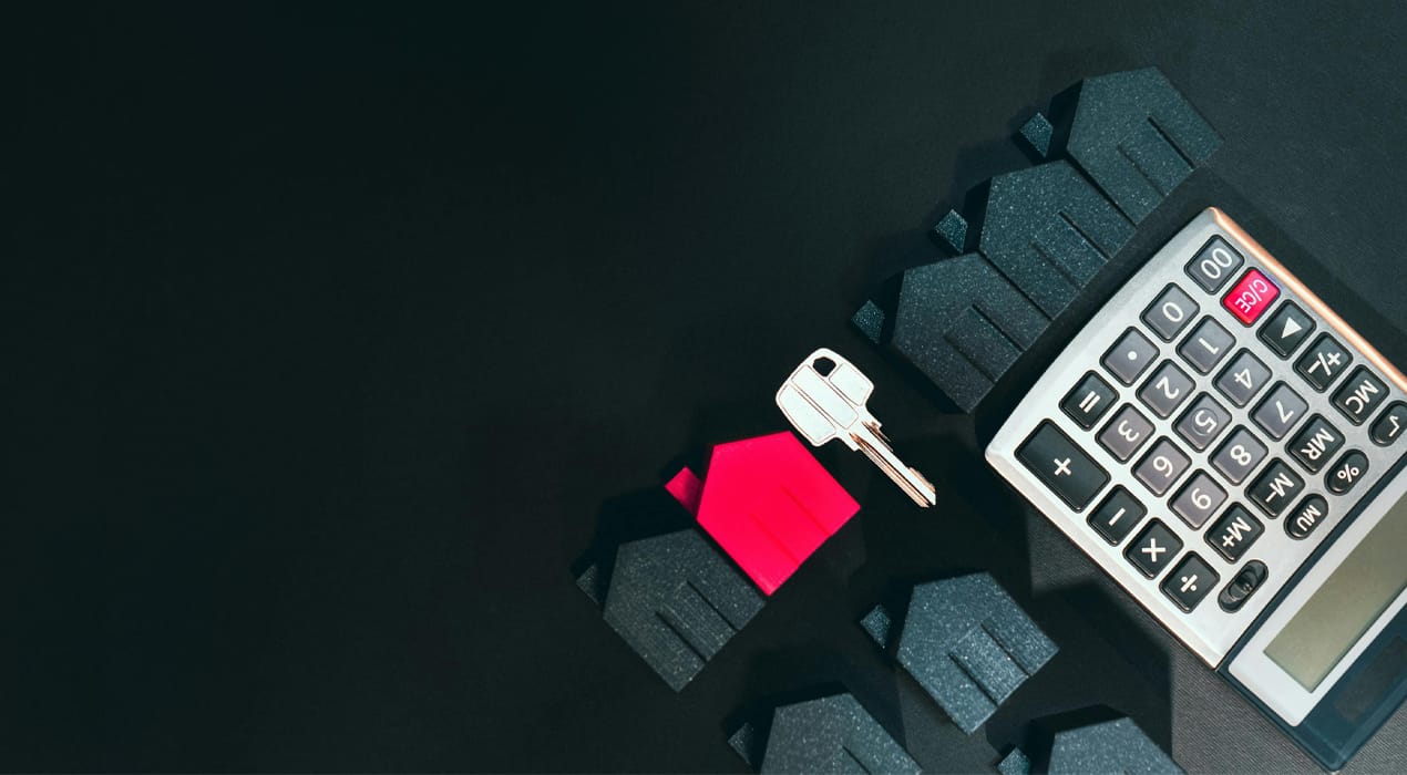 Row of mini model houses, a key and a calculator laid out on a black surface.