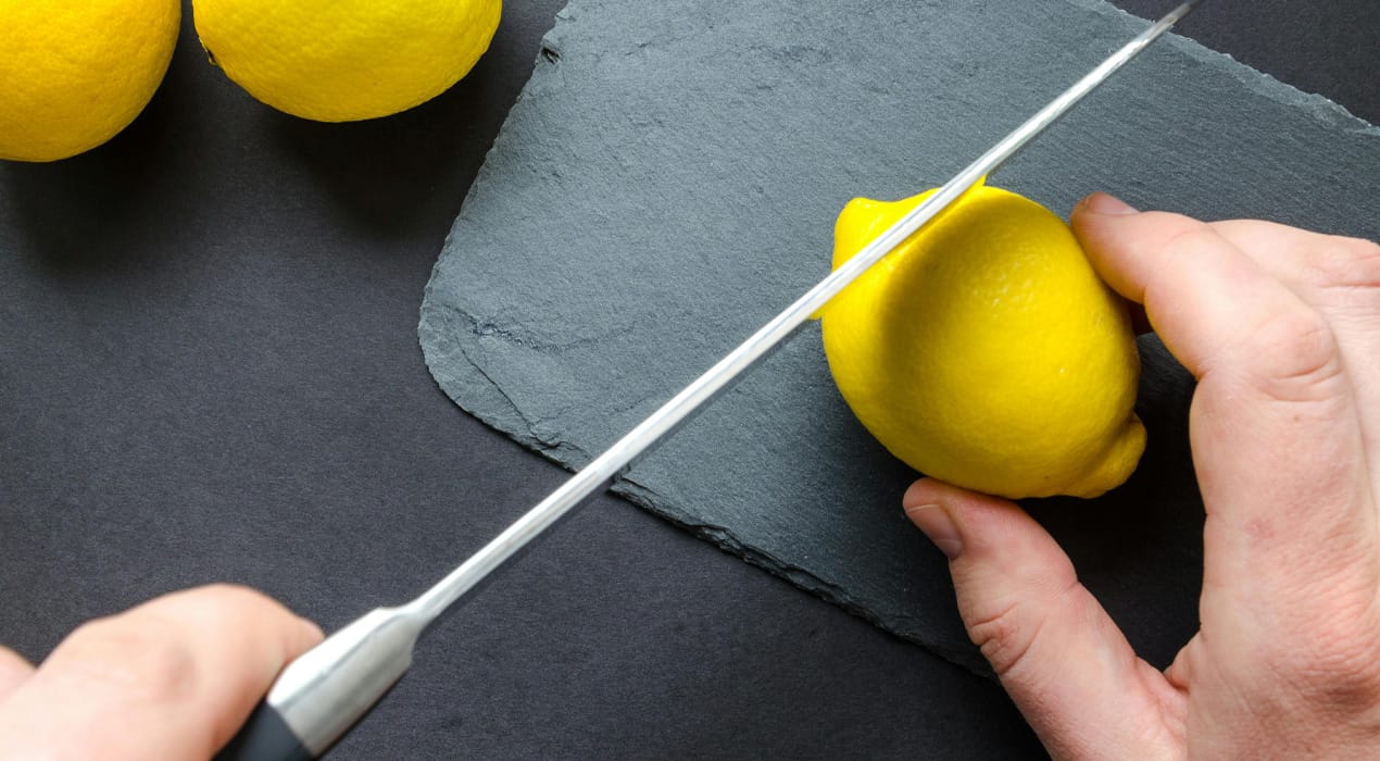 Close up of a person cutting thin slices of a lemon on a chopping board