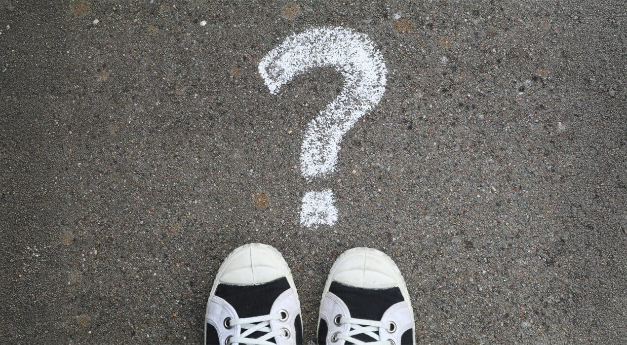 A pair of sneaker shoes on the floor in front of a large white chalk question mark.