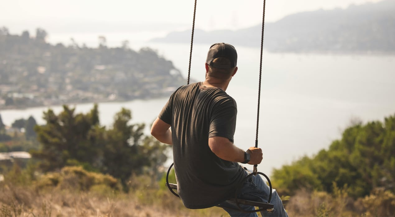 Man sitting on a swing on top of a hill looking out over a bay of water