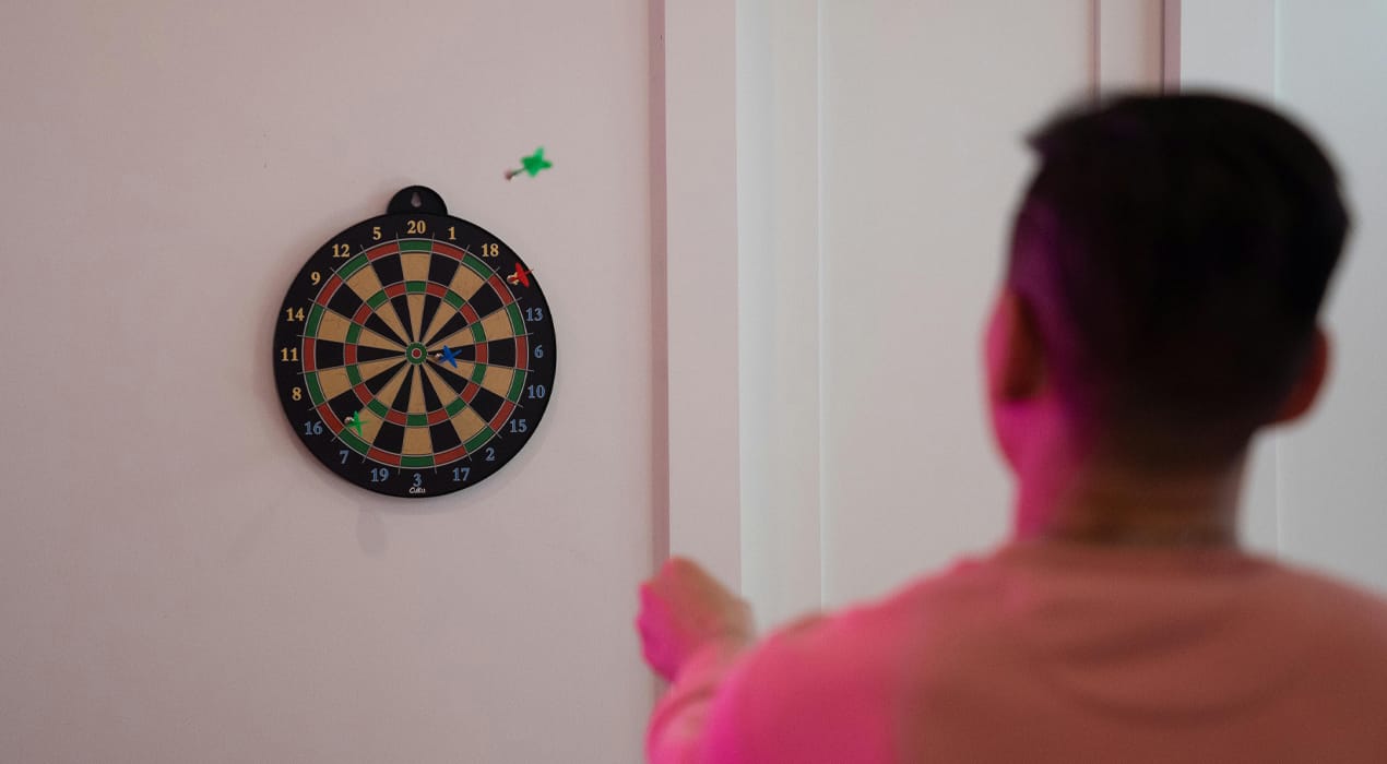Man playing darts, with one dart lodged in the wall next to the board