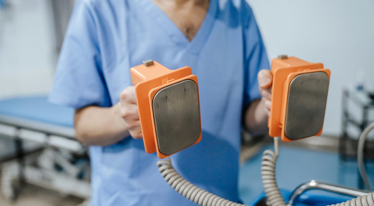 Doctor or nurse in light blue scrubs holding a pair of difibrillator paddles