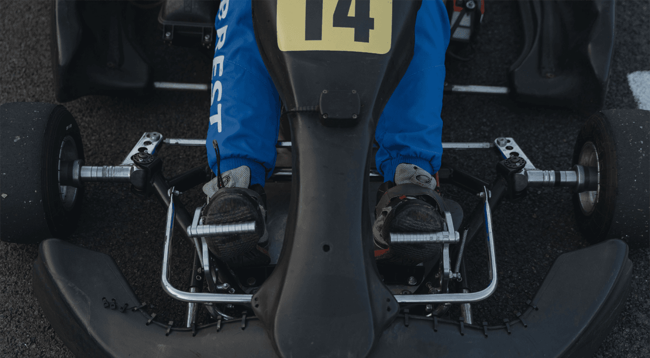 Close up view of a persons legs sitting in a go kart with feet on pedals either side of the steering column