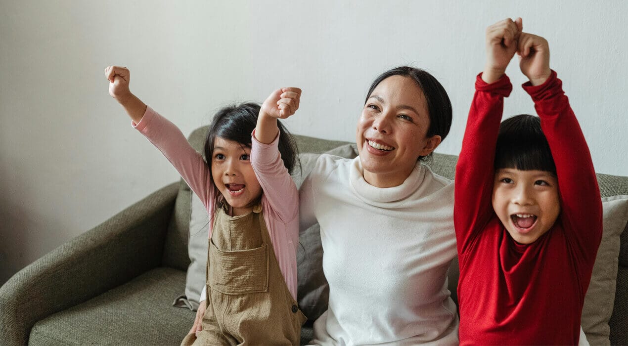 A mum and two young kids sitting on the couch, cheering in celebration