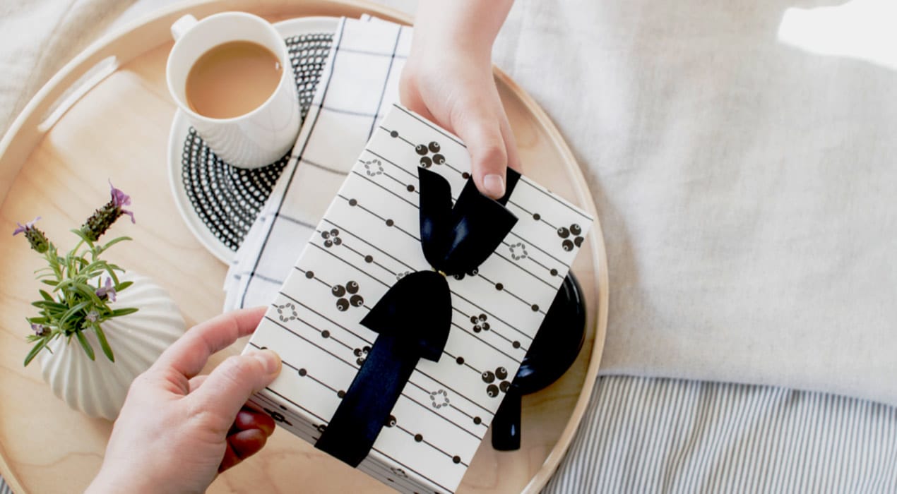 Close up of one person handing a wrapped gift to another person, over a coffee table