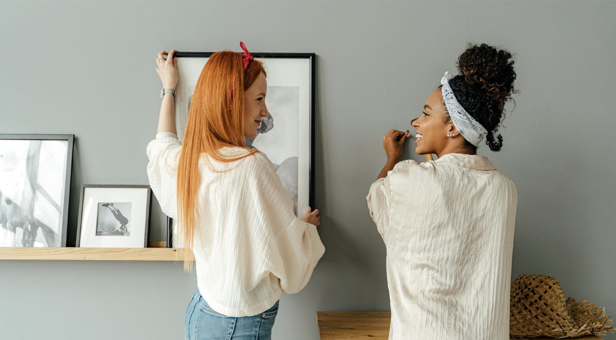 Two young women hanging pictures on a wall