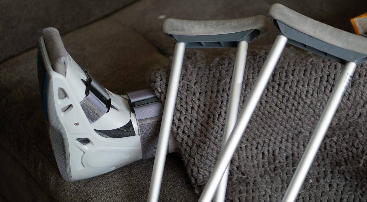 Close up image of a foot in a moon boot, with crutches resting across it
